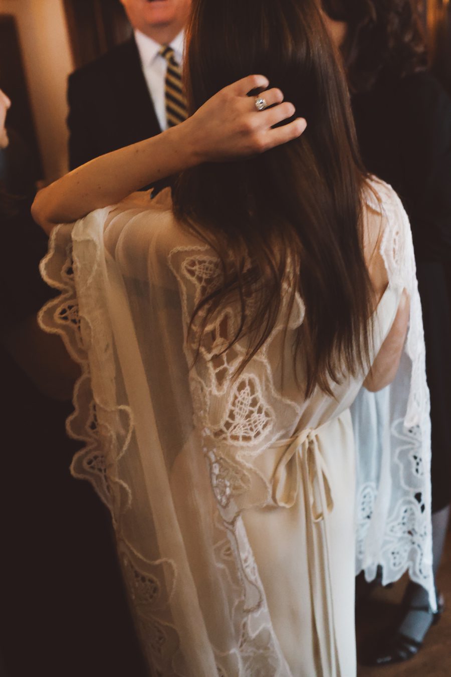 Woman with long hair wearing lace dress is being touched on the head by another person at a formal event.