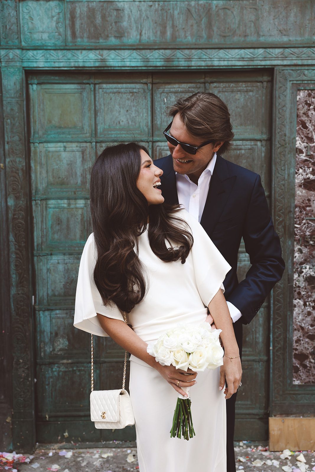 A couple at the iconic green door of the city clerk's office on worth street they are looking chic and she wears a ysl bag and white roses